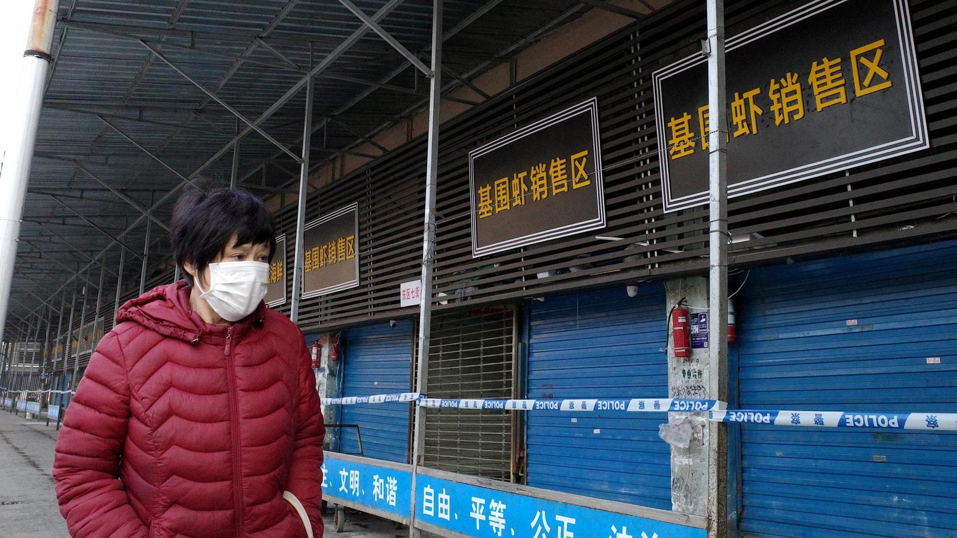 Eine Frau mit Mundschutz steht vor dem geschlossenen Markt in Wuhan. Eine Frau mit Mundschutz steht vor dem geschlossenen Markt in Wuhan.