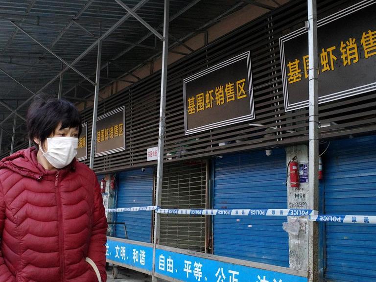 Eine Frau mit Mundschutz steht vor dem geschlossenen Markt in Wuhan.