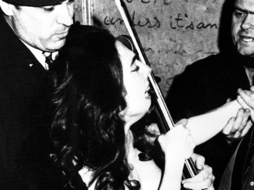 Die Cellistin Charlotte Moorman wird unter Protest von der Polizei abgeführt, weil sie ohne Oberbekleidung ein Konzert in einem kleinen Off-Broadway-Theater gegeben hat. Auf dem Programm stand "Melodie-Elegie des Erinnyes" von Jules Massenet.