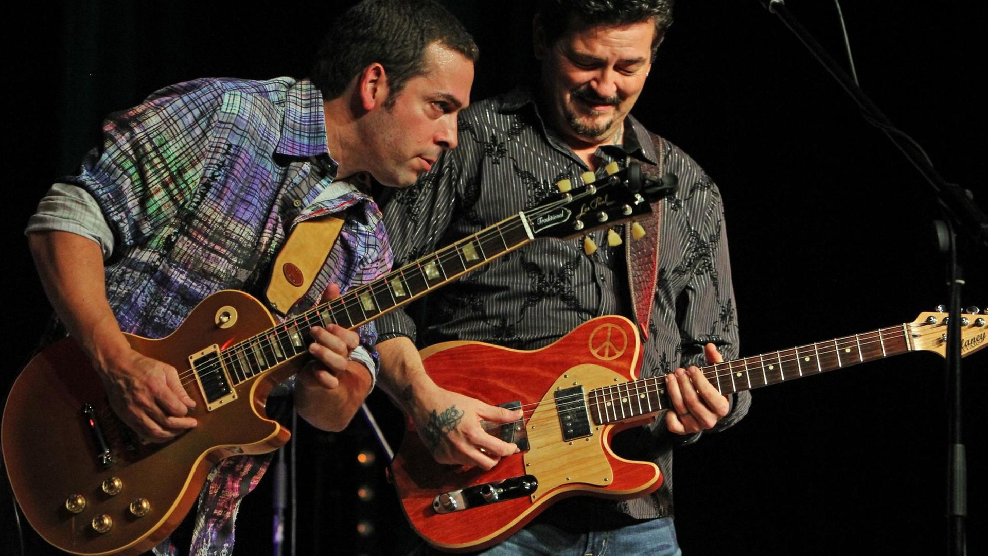 Zwei Männer stehen auf einer Bühne und spielen Gitarre Zwei Männer stehen auf einer Bühne und spielen Gitarre