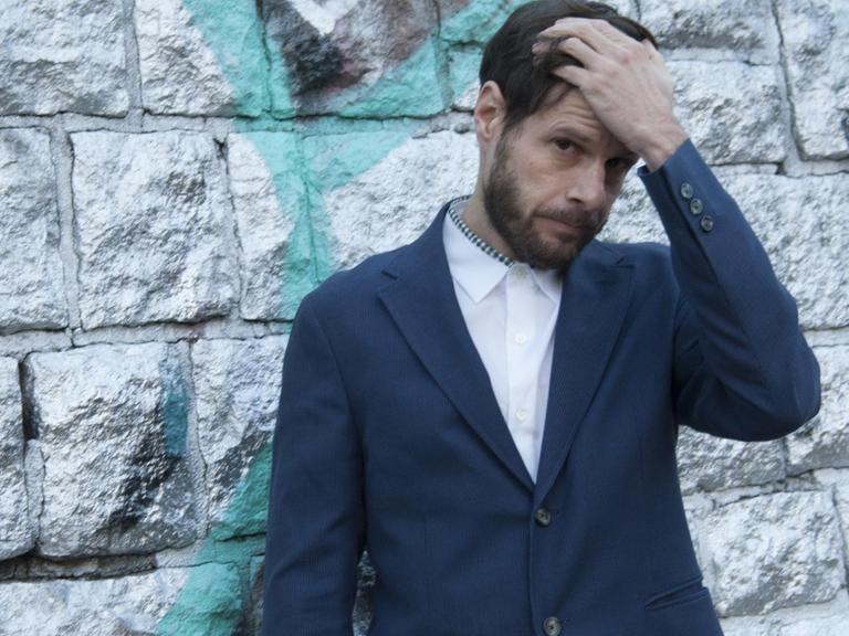 Der Feature-Autor Christian Lerch steht vor einer Wand und fasst sich in die Haare.