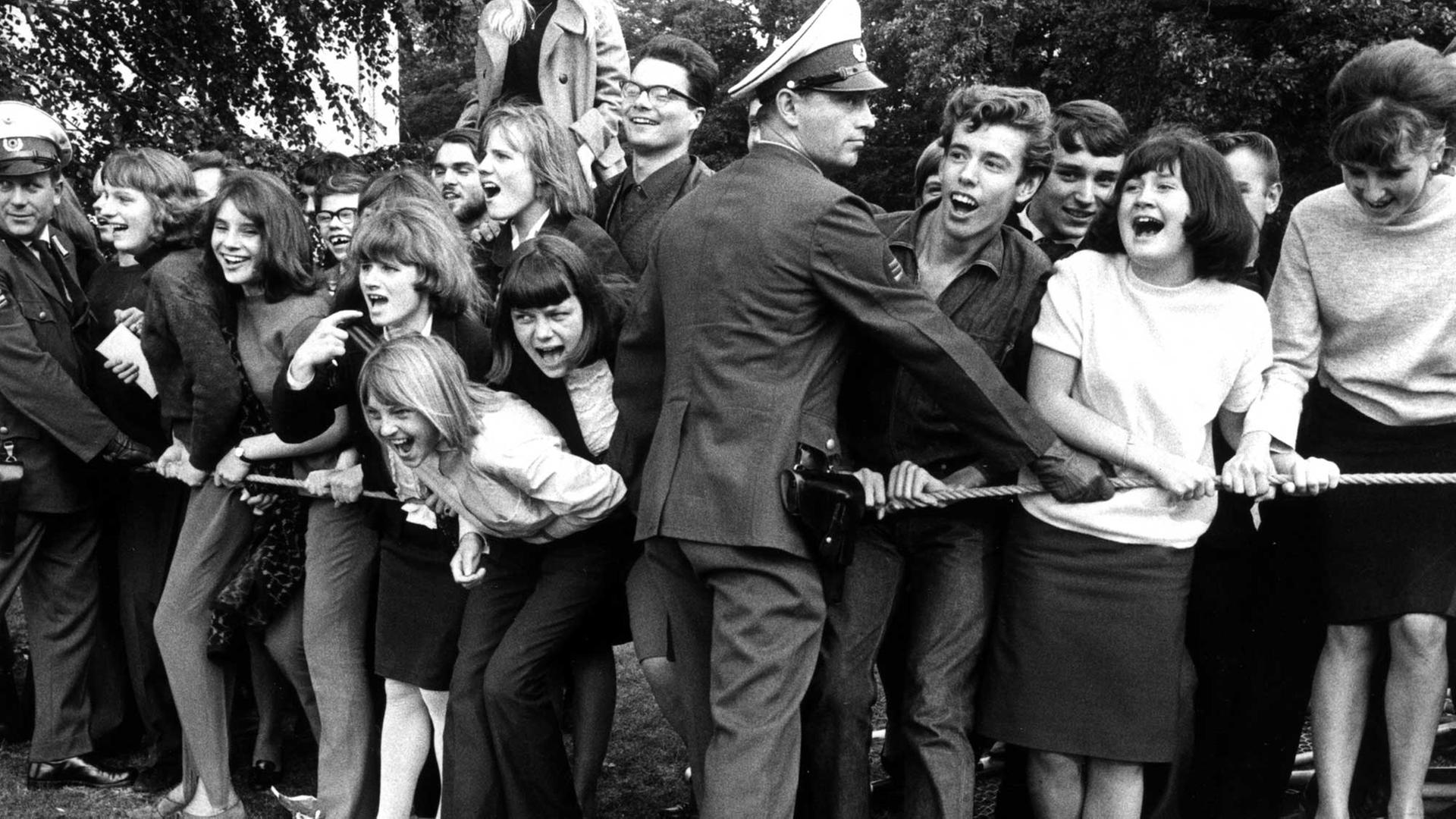 Begeisterte Fans begrüßten am 15.09.1965 auf dem Flughafen Berlin-Tegel die "Rolling Stones" vor ihrem Konzert in der Waldbühne. Polizisten halten die Menge mit einer Absperrung zurück. Begeisterte Fans begrüßten am 15.09.1965 auf dem Flughafen Berlin-Tegel die "Rolling Stones" vor ihrem Konzert in der Waldbühne. Polizisten halten die Menge mit einer Absperrung zurück.