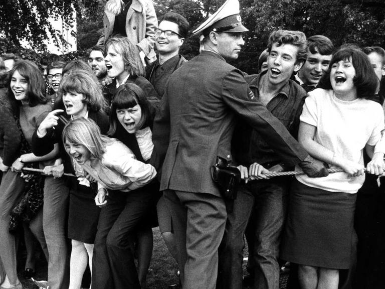 Begeisterte Fans begrüßten am 15.09.1965 auf dem Flughafen Berlin-Tegel die "Rolling Stones" vor ihrem Konzert in der Waldbühne. Polizisten halten die Menge mit einer Absperrung zurück.