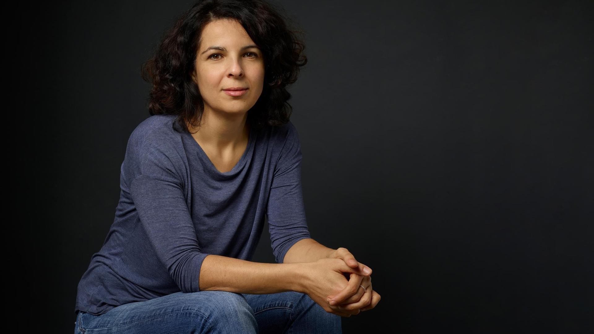 Dilek Güngör sitzt vor einem dunklen Hintergrund und schaut in die Kamera. Dilek Güngör sitzt vor einem dunklen Hintergrund und schaut in die Kamera.