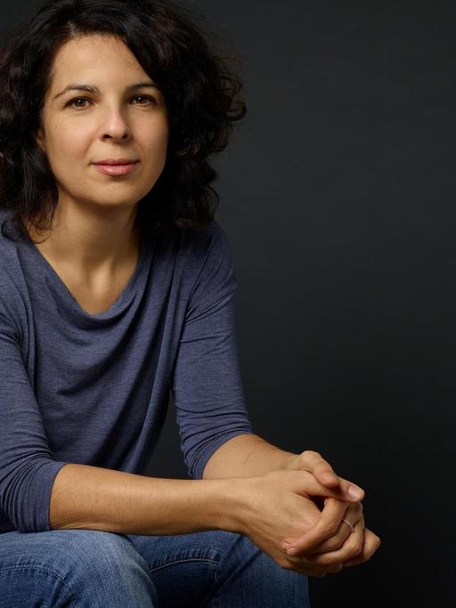 Dilek Güngör sitzt vor einem dunklen Hintergrund und schaut in die Kamera.