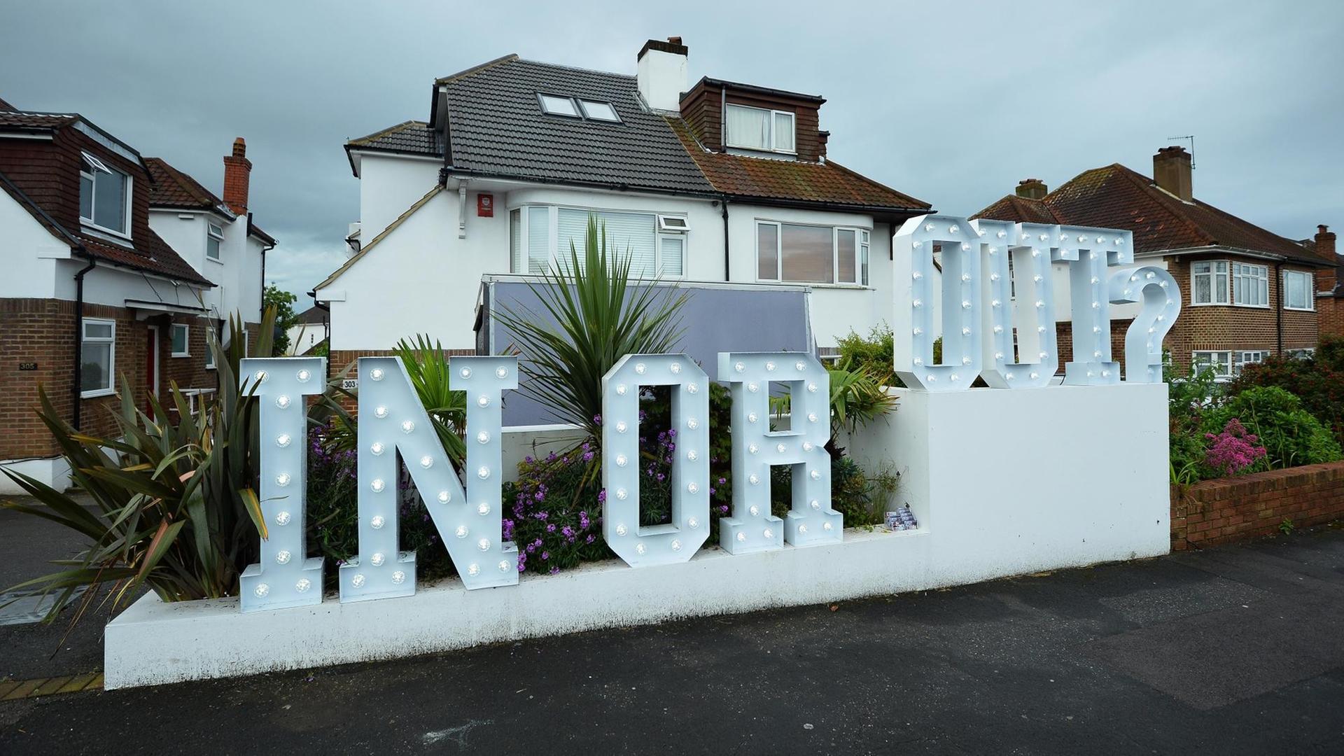 Ein beleuchteter "In or Out"-Schriftzug vor einem Haus. Ein beleuchteter "In or Out"-Schriftzug vor einem Haus.