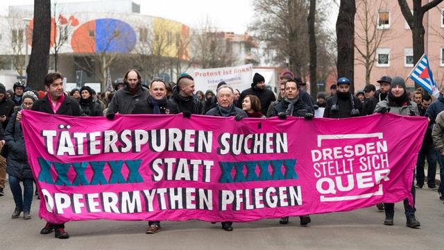 10.02.2018, Sachsen, Dresden: Teilnehmer einer Kundgebung des Bündnises Dresden Nazifrei stehen hinter einem Banner mit der Aufschrift "Täterspuren suchen statt Opfermythen pflegen".