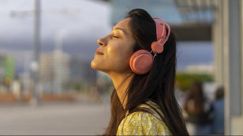 Eine junge Frau mit Kopfhörern und geschlossenen Augen scheint in entspannter Stimmung zu sein