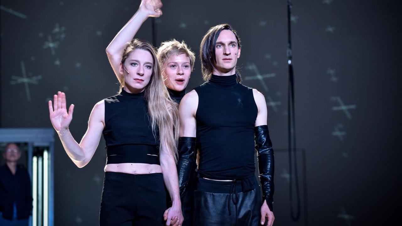 Kathleen Morgeneyer, Luise Hart und Thorsten Hierse stehen schwarz gekleidet auf der Bühne und halten jeweils eine Hand hoch.