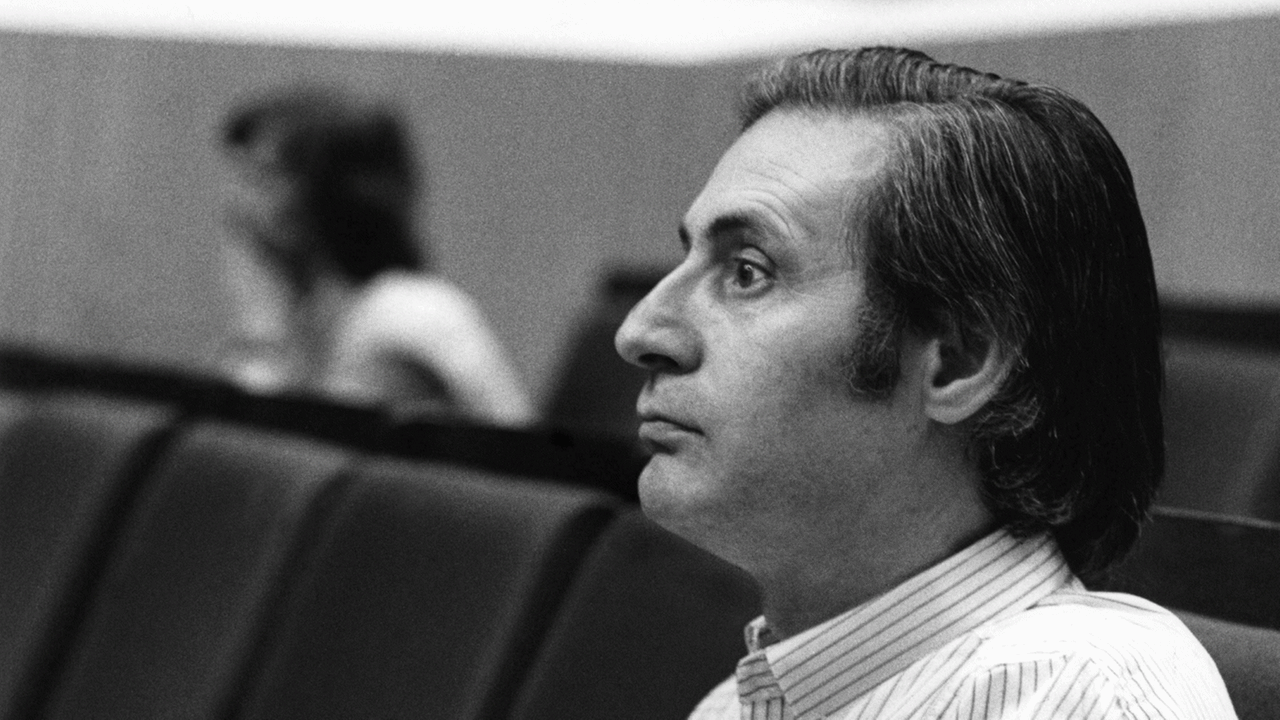 Der Komponist Alfred Schnittke, im Profil zu sehen, wie er in einem sonst fast leeren Auditorium sitzt und zuhört.