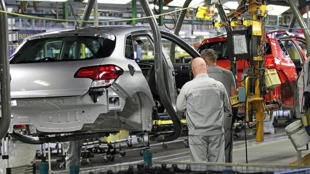 Eine Autokarosserie hängt in einer Werkshalle des Autoherstellers PSA im französischen Mülhausen an einem Transportband. Davor steht ein Arbeiter in grauer Kleidung.