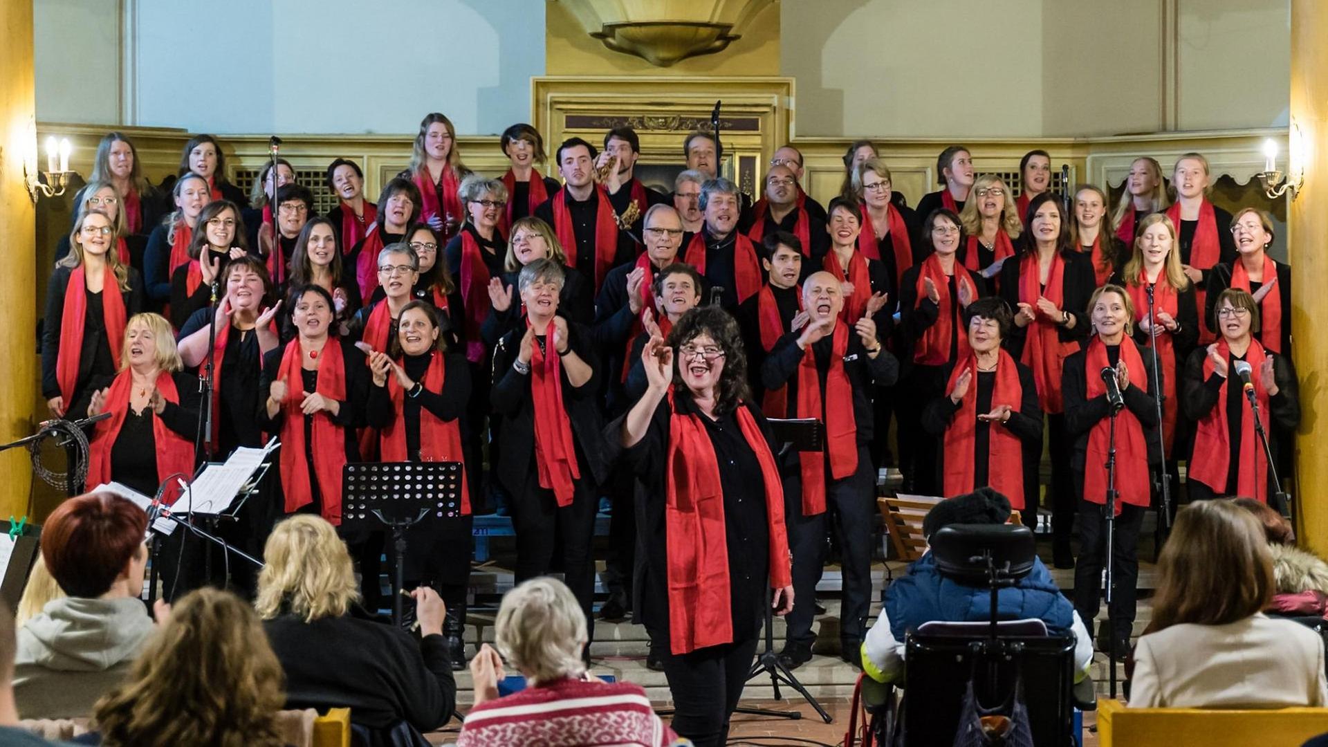 Der Chor singt bei einem Auftritt in der Kirche. Die Chorleiterin wendet sich schwungvoll dem Publikum zu. Der Chor singt bei einem Auftritt in der Kirche. Die Chorleiterin wendet sich schwungvoll dem Publikum zu.