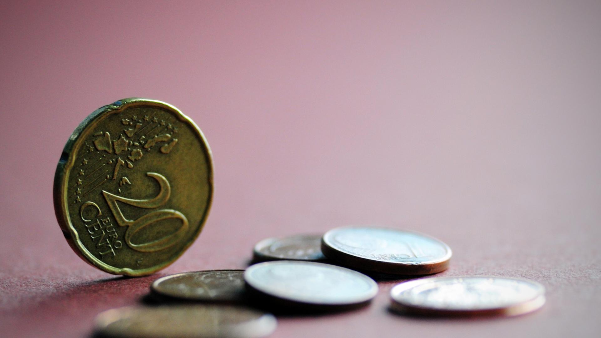 Mehrere Euro-Münzen liegen auf einem farbigen Papier, eine 20-Cent-Münze steht aufrecht Mehrere Euro-Münzen liegen auf einem farbigen Papier, eine 20-Cent-Münze steht aufrecht