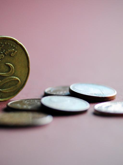 Mehrere Euro-Münzen liegen auf einem farbigen Papier, eine 20-Cent-Münze steht aufrecht