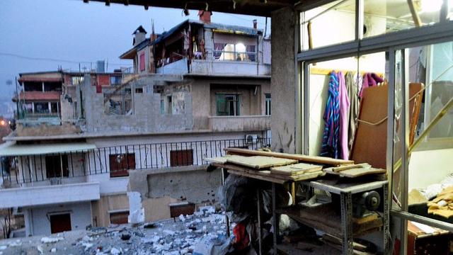 Blick in ein zerstörtes Haus im Stadtviertel Al-Mazza in Damaskus (Syrien) am 25. Januar 2015. Im Vordergrund steht ein Regal, im Hintergrund hängen in einem Zimmer Kleider.