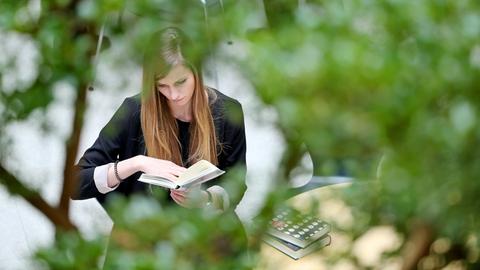 Eine junge Frau liest unter einem Baum ein Buch.