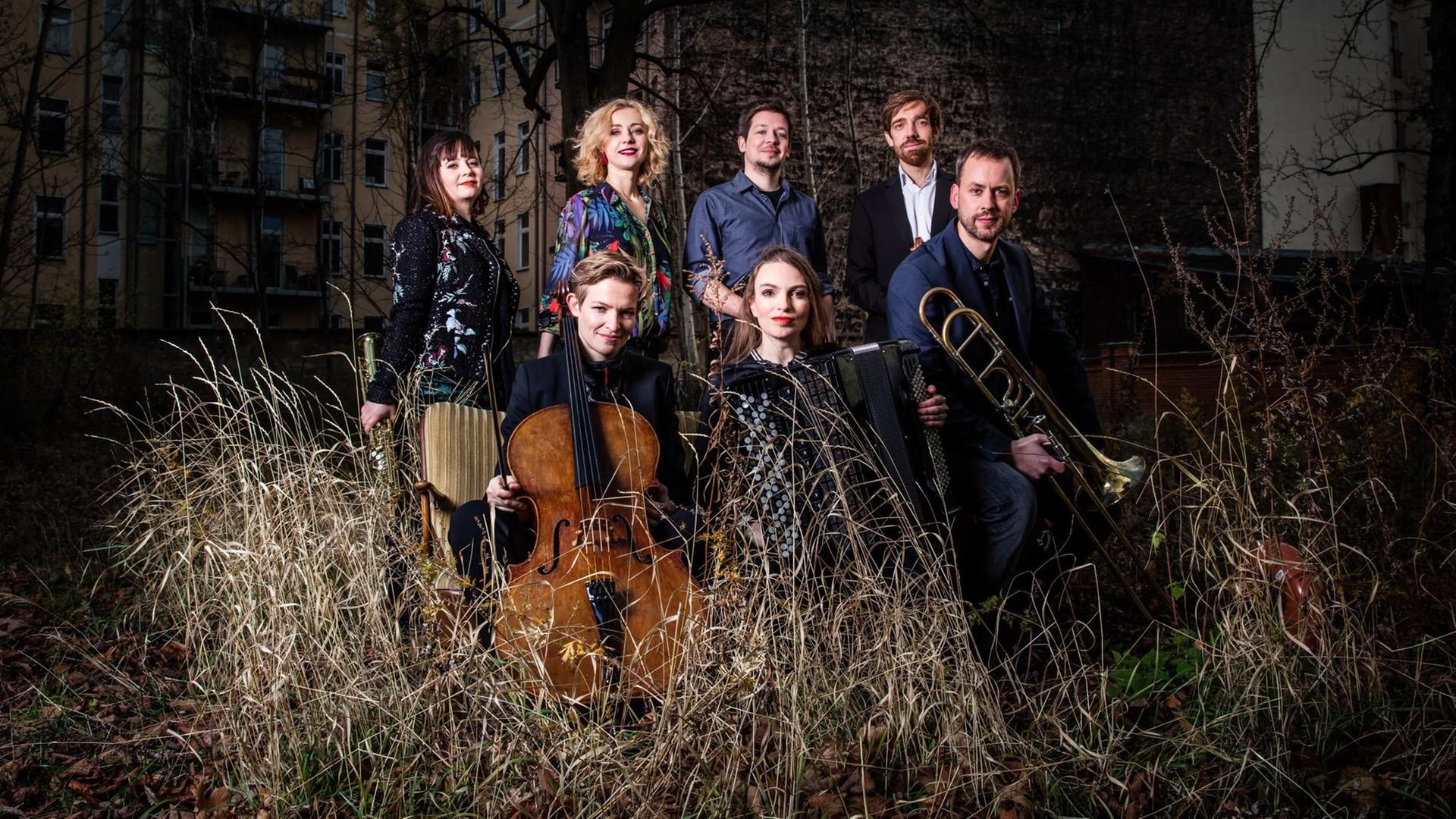 Eine Gruppe von Musikern stehen mit ihren Instrumenten im hohen Gras vor einer Häuserfront Eine Gruppe von Musikern stehen mit ihren Instrumenten im hohen Gras vor einer Häuserfront