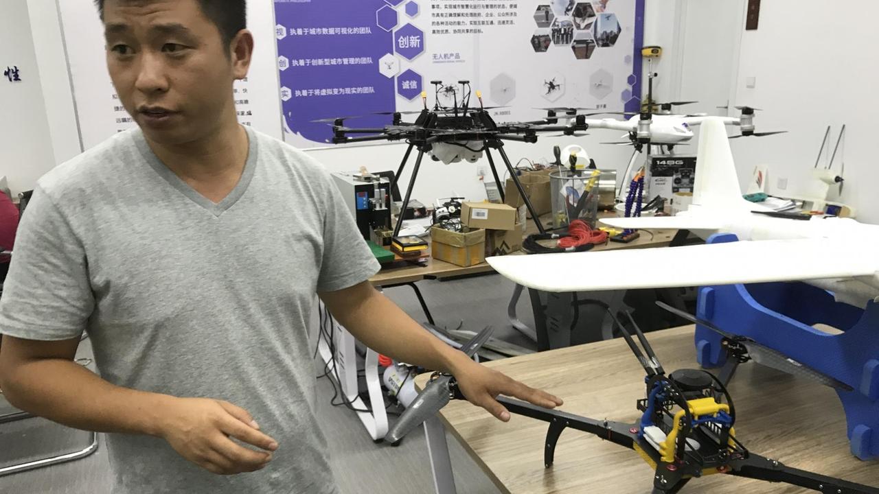 Der studierte Luftfahrtingenieur Wen Yidao entwickelt hier mit fünf Kollegen Hightech-Drohnen zum Filmen, Fotografieren, Kontrollieren und Überwachen. Er trägt ein graues T-Shirt und zeigt auf eine schwarze Drohne.