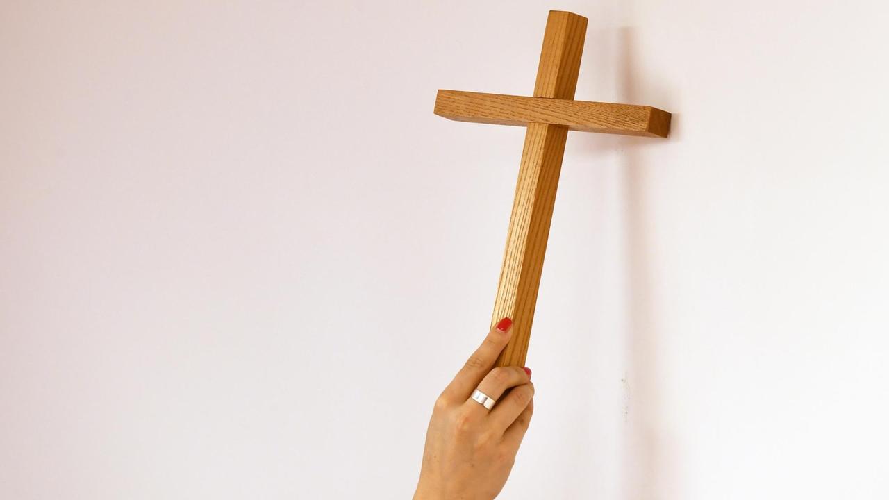 Ein Kreuz wird an eine Wand gehängt. Ein Kreuz wird an eine Wand gehängt.