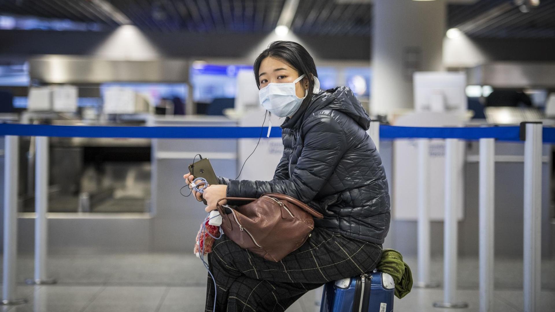 Eine Passagierin warten mit Atemschutzmaske und ihrem Handy am Check-In Schalter auf dem Frankfurter Flughafen. Eine Passagierin warten mit Atemschutzmaske und ihrem Handy am Check-In Schalter auf dem Frankfurter Flughafen.