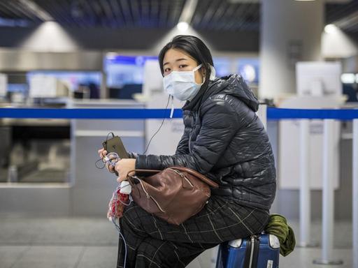Eine Passagierin warten mit Atemschutzmaske und ihrem Handy am Check-In Schalter auf dem Frankfurter Flughafen.