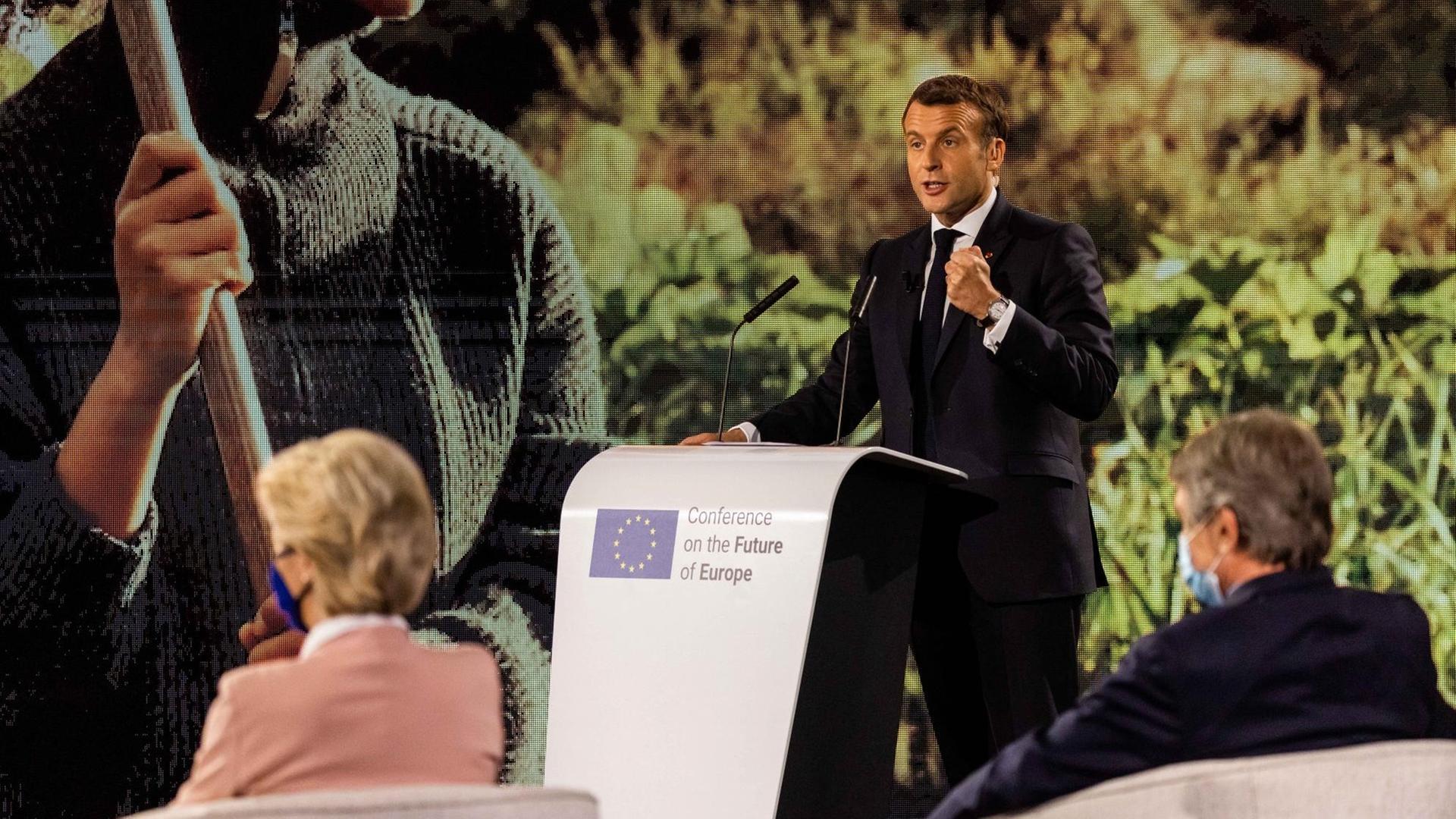 Emmanuel Macron (M, En Marche), Staatspräsident von Frankreich, spricht während der Eröffnungsveranstaltung der Konferenz zur Zukunft Europas im Gebäude des Europäischen Parlaments während Ursula von der Leyen (l, CDU, Fraktion EVP), Präsidentin der Europäischen Kommission, und David Sassoli (r, PD, Fraktion S&D), Präsident des Europäischen Parlaments, im Vordergrund sitzen. Emmanuel Macron (M, En Marche), Staatspräsident von Frankreich, spricht während der Eröffnungsveranstaltung der Konferenz zur Zukunft Europas im Gebäude des Europäischen Parlaments während Ursula von der Leyen (l, CDU, Fraktion EVP), Präsidentin der Europäischen Kommission, und David Sassoli (r, PD, Fraktion S&D), Präsident des Europäischen Parlaments, im Vordergrund sitzen.