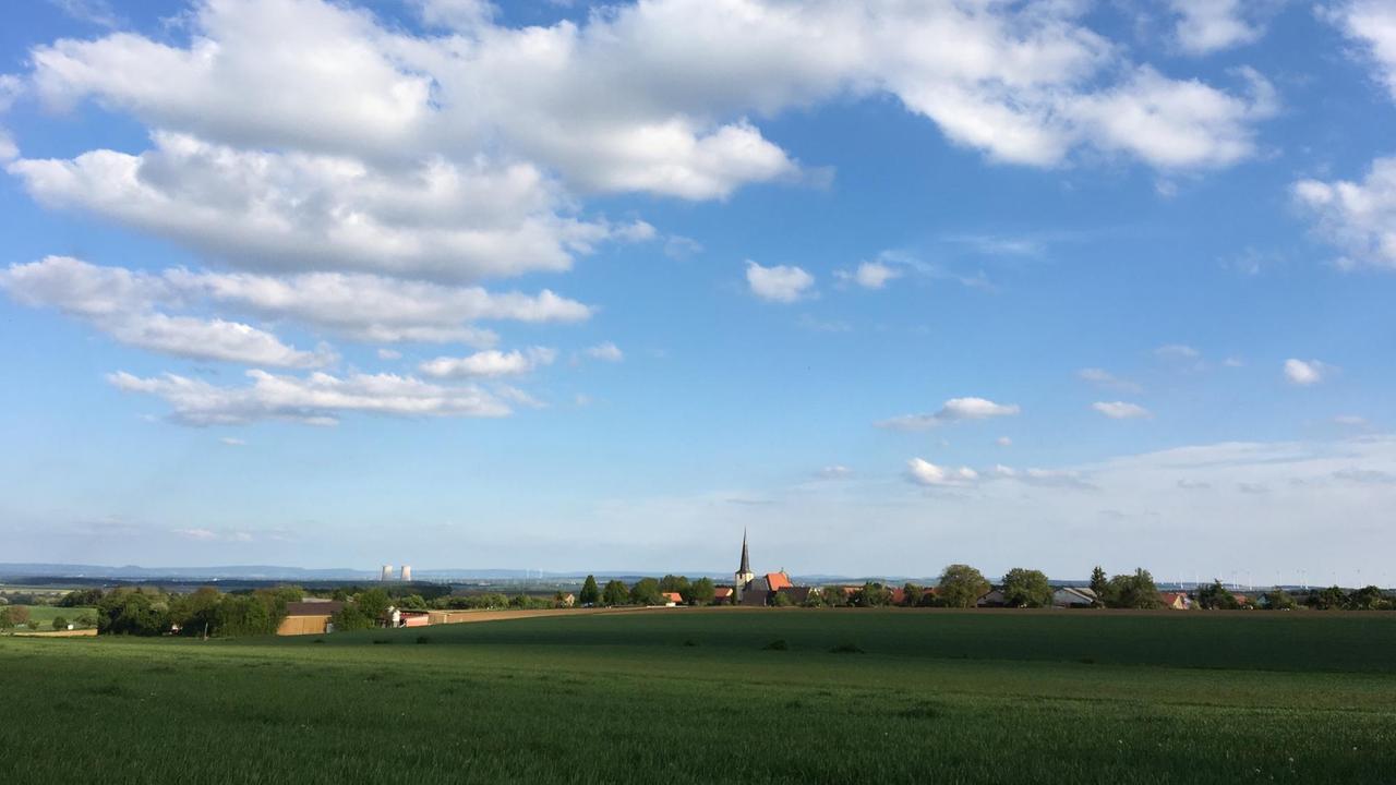 Landschaftsaufnahme eines Getreidefeldes, am Horizont eine Kirche und ein AKW.