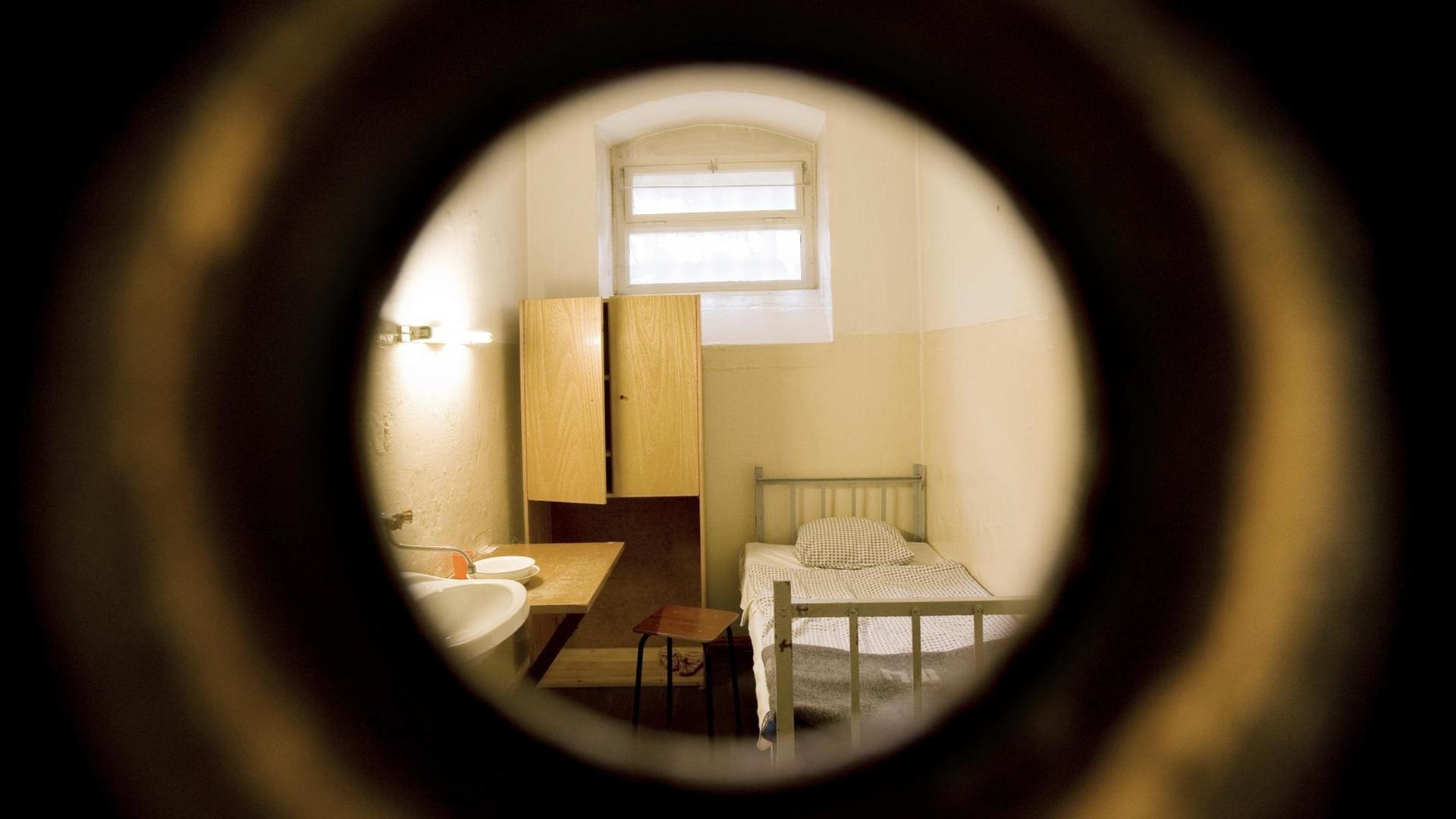 Blick auf einer Einzelzelle durch eine kleine runde Gefängnistüröffnung.