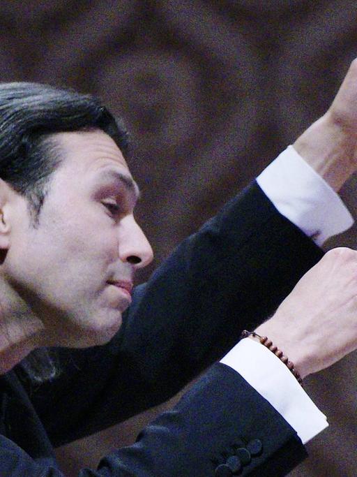 Der Dirigent im Profil, beide Hände für das Orchester erhoben.