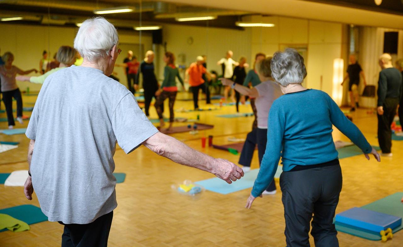 Senioren mit ausgetreckten Armen machen während einer Sportstunde eine Gleichgewichtsübung.