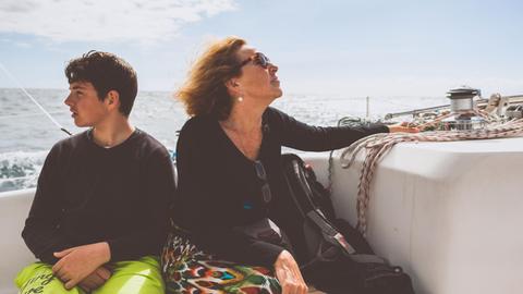 Ein Jugendlicher und sein Mutter sitzen auf an Bord eines Schiffes und schauen jeweils in einer andere Richtung.