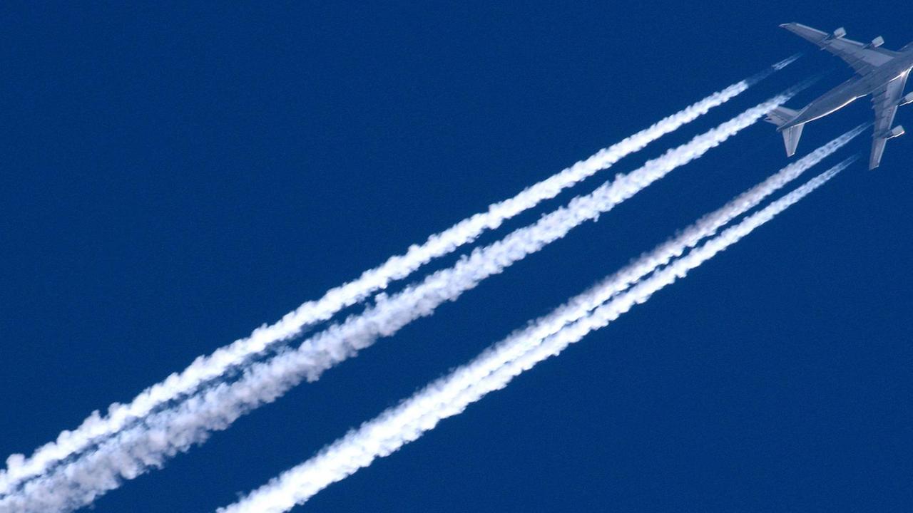 Ein Passagierjet fliegt bei klarer Sicht am blauen Himmel und zieht vier lange Kondenzstreifen hinter sich her.