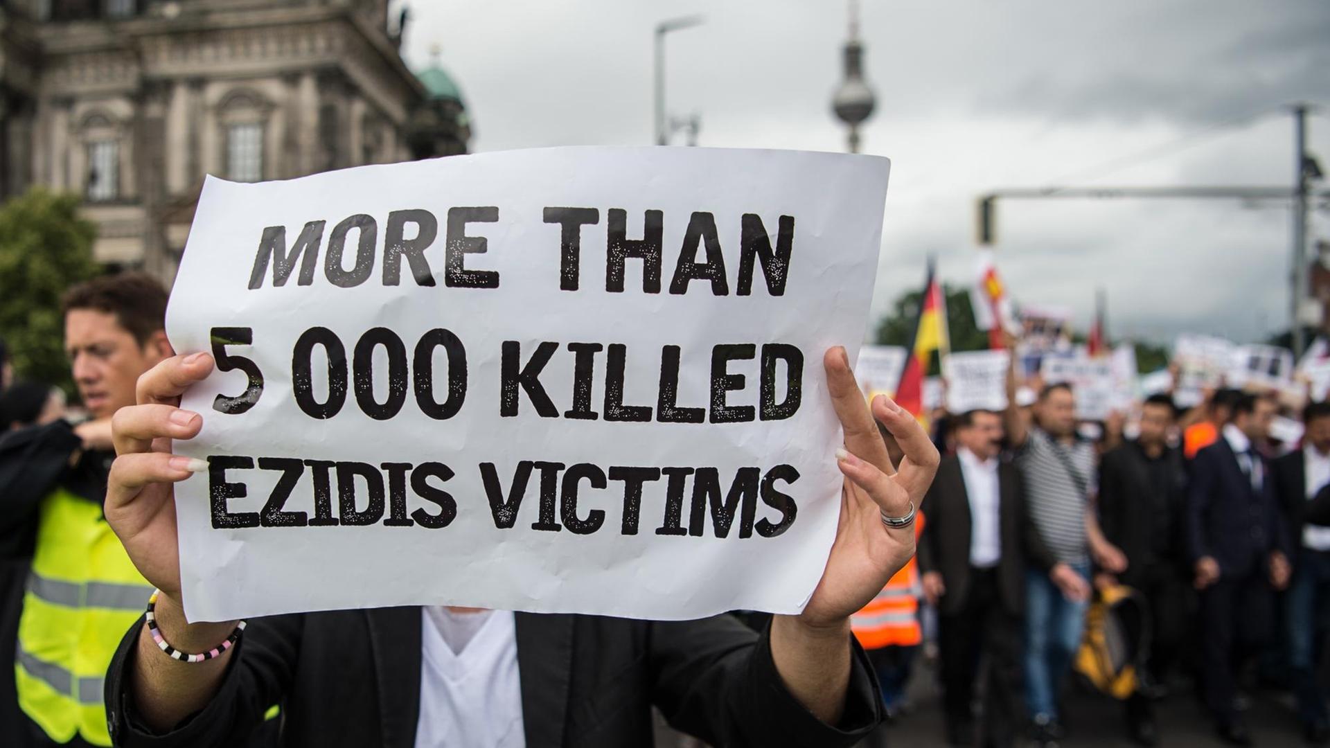 Ein Mann hält ein Schild mit der Aufschrift «MORE THAN 5 000 KILLED EZIDIS VICTIMS» («über 5000 getötete jesidische Opfer») am 03.08.2016 in Berlin bei einem Gedenkmarsch anlässlich des Überfalls der Terrororgruppe «Islamischer Staat» (IS) auf die religiösen und ethischen Minderheiten im Nordirak. Ein Mann hält ein Schild mit der Aufschrift «MORE THAN 5 000 KILLED EZIDIS VICTIMS» («über 5000 getötete jesidische Opfer») am 03.08.2016 in Berlin bei einem Gedenkmarsch anlässlich des Überfalls der Terrororgruppe «Islamischer Staat» (IS) auf die religiösen und ethischen Minderheiten im Nordirak.