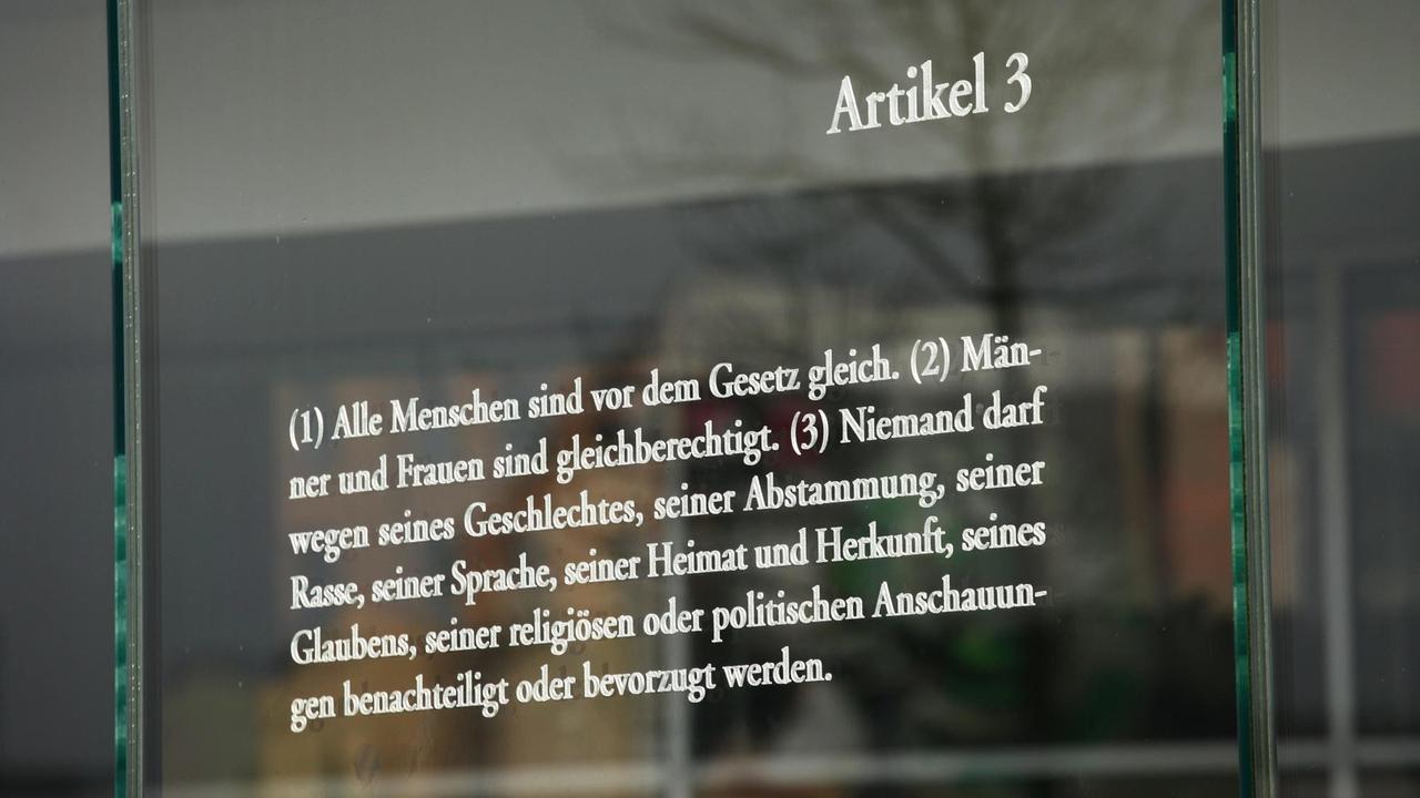Der Artikel 3 des Grundgesetzes zur Gleichheit von Männern und Frauen steht auf einer Platte aus Glas, aufgenommen am 2016 in Berlin im Bezirk Mitte im Regierungsviertel. Nach Artikel 3 darf auch Niemand wegen seiner Rasse, Herkunft oder politischen Anschauungen diskriminiert werden. An der Promenade der Spree in Berlin verbinden 19 jeweils drei Meter hohe Glasscheiben einen Außenhof des Jakob-Kaiser-Hauses mit dem Uferbereich. Mit Laser sind in die Glasscheiben die 19 Grundrechtsartikel des deutschen Grundgesetzes eingegraviert. Die Installation ist ein "Grundgesetz 49" benanntes Werk des israelischen Künstlers Dani Karavan. Der Artikel 3 des Grundgesetzes zur Gleichheit von Männern und Frauen steht auf einer Platte aus Glas, aufgenommen am 2016 in Berlin im Bezirk Mitte im Regierungsviertel. Nach Artikel 3 darf auch Niemand wegen seiner Rasse, Herkunft oder politischen Anschauungen diskriminiert werden. An der Promenade der Spree in Berlin verbinden 19 jeweils drei Meter hohe Glasscheiben einen Außenhof des Jakob-Kaiser-Hauses mit dem Uferbereich. Mit Laser sind in die Glasscheiben die 19 Grundrechtsartikel des deutschen Grundgesetzes eingegraviert. Die Installation ist ein "Grundgesetz 49" benanntes Werk des israelischen Künstlers Dani Karavan.