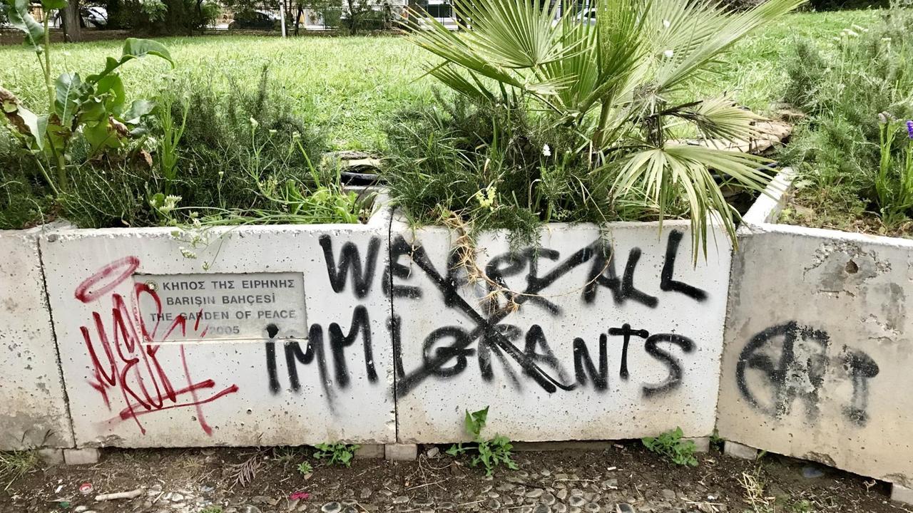 Graffiti an einer Mauer in Zypern: der Spruch "We are all immigrants" ist schwarzer Farbe durchgestrichen. Graffiti an einer Mauer in Zypern: der Spruch "We are all immigrants" ist schwarzer Farbe durchgestrichen.