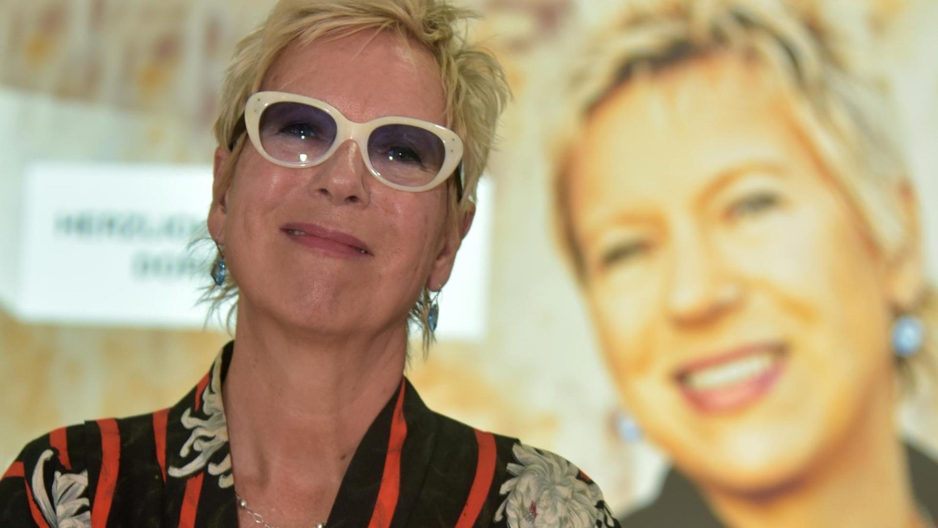 Das Foto zeigt die Regisseurin Doris Dörrie, die im Filmmuseum Frankfurt vor einem Plakat mit ihrem Konterfei posiert.