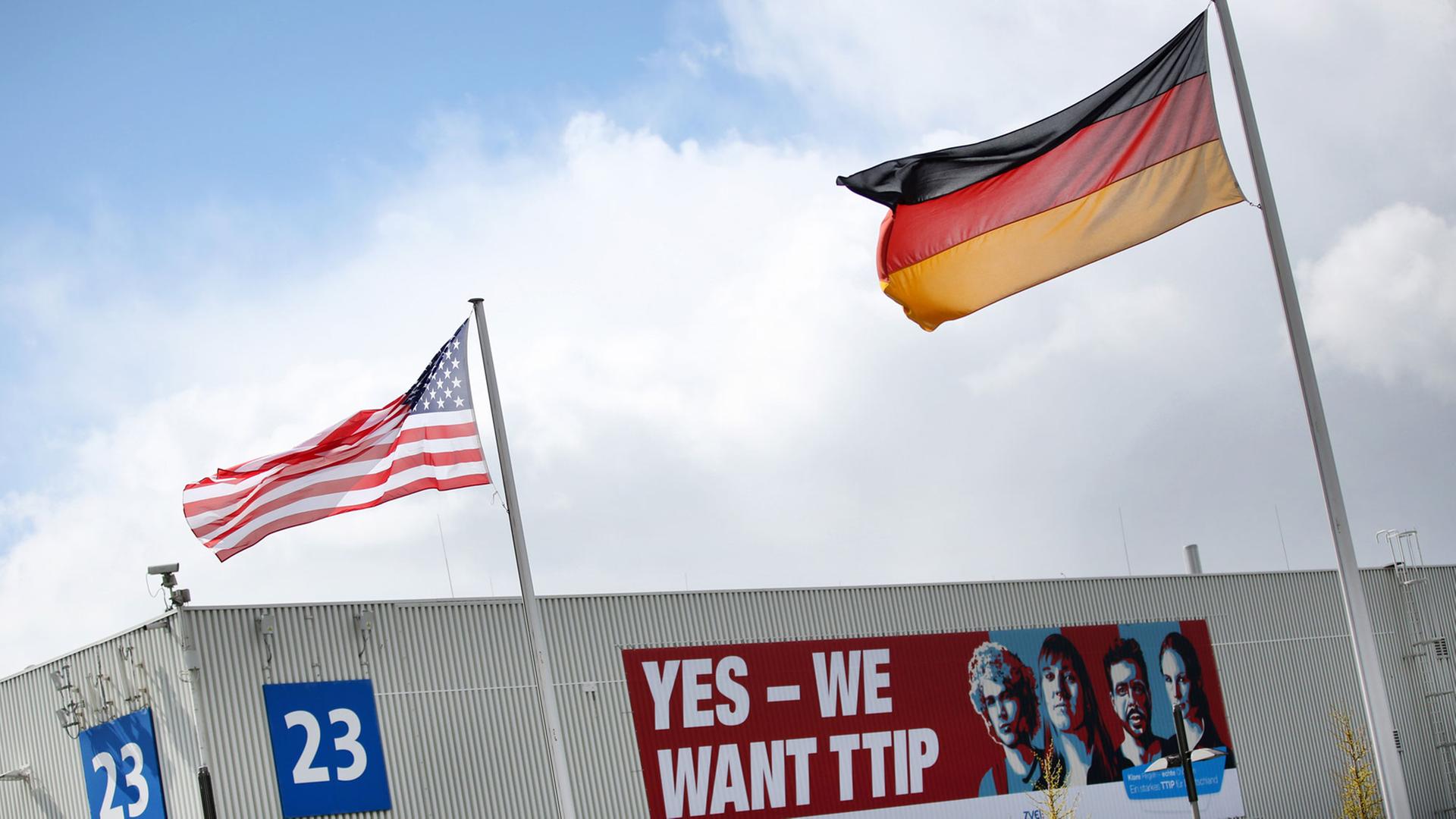 Eine amerikanische Flagge und eine deutsche Flagge wehen am 24.04.2016 auf dem Gelände der Hannover Messe in Hannover (Niedersachsen) vor einem Plakat mit der Aufschrift "Yes - We want TTIP". Die weltgrößte Industriemesse Hannover Messe wird am 24. April von US-Präsident Obama eröffnet. Partnerland der Messe sind in diesem Jahr die USA. Eine amerikanische Flagge und eine deutsche Flagge wehen am 24.04.2016 auf dem Gelände der Hannover Messe in Hannover (Niedersachsen) vor einem Plakat mit der Aufschrift "Yes - We want TTIP". Die weltgrößte Industriemesse Hannover Messe wird am 24. April von US-Präsident Obama eröffnet. Partnerland der Messe sind in diesem Jahr die USA.