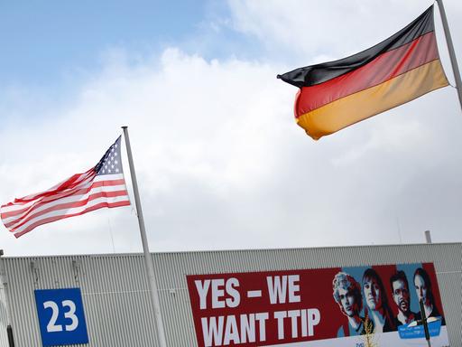 Eine amerikanische Flagge und eine deutsche Flagge wehen am 24.04.2016 auf dem Gelände der Hannover Messe in Hannover (Niedersachsen) vor einem Plakat mit der Aufschrift "Yes - We want TTIP". Die weltgrößte Industriemesse Hannover Messe wird am 24. April von US-Präsident Obama eröffnet. Partnerland der Messe sind in diesem Jahr die USA.