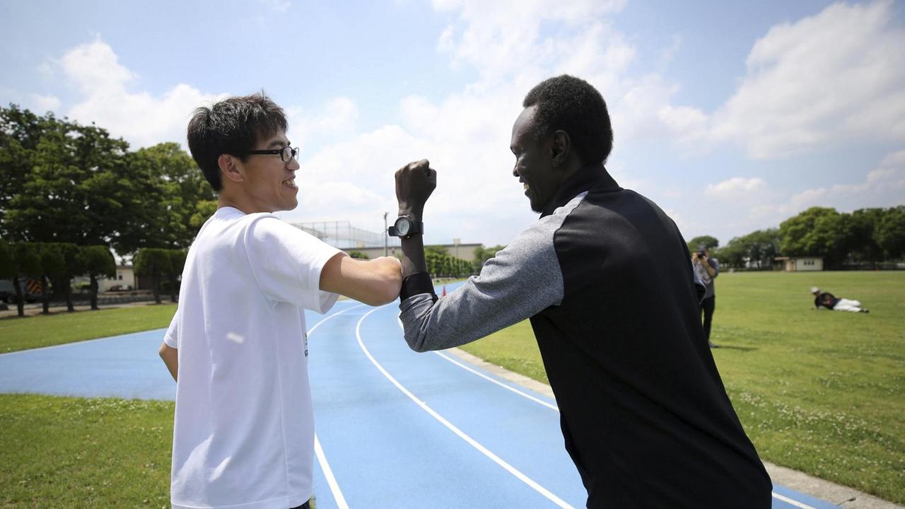 Der südsudanesische Leichtathlet Kutjang Michael Machiek Ting grüßt seinen japanischen Coach mit dem "Corona-Gruß". Der südsudanesische Leichtathlet Kutjang Michael Machiek Ting grüßt seinen japanischen Coach mit dem "Corona-Gruß".