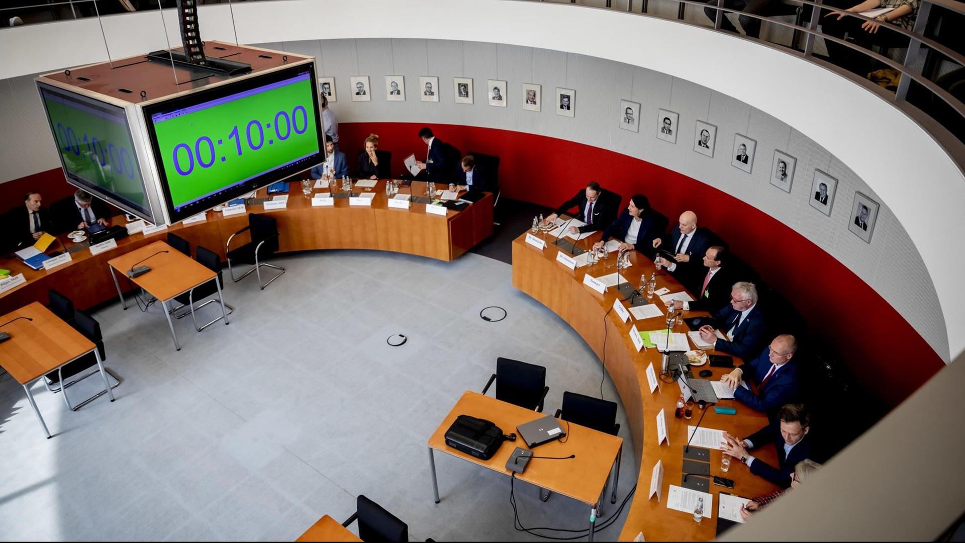 Das Bild ist vom Besucherrang aus gemacht; man sieht unten die Teilnehmer an halbrunden Tischen und oben Zuschauer auf der Tribüne. Von der Decke hängt eine viereckige Digitaluhr herab. Das Bild ist vom Besucherrang aus gemacht; man sieht unten die Teilnehmer an halbrunden Tischen und oben Zuschauer auf der Tribüne. Von der Decke hängt eine viereckige Digitaluhr herab.