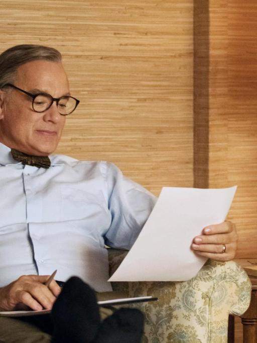 Tom Hanks sitzt in einer Filmszene als Fred Rogers auf einem Sofa.