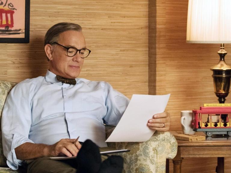 Tom Hanks sitzt in einer Filmszene als Fred Rogers auf einem Sofa.