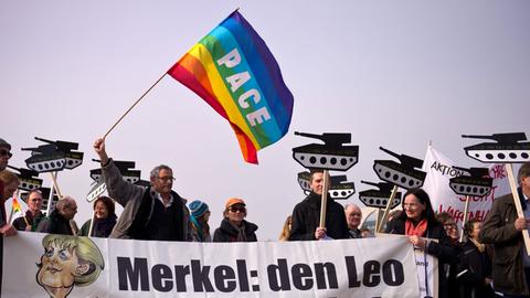 Einige Menschen protestieren am 26.02.2014 vor dem Reichstag in Berlin mit Transparenten in Form eines Panzers und einem Plakat mit der Aufschrift "Merkel: den Leo an die Kette" bei einer Kundgebung gegen die deutschen Rüstungsexporte.