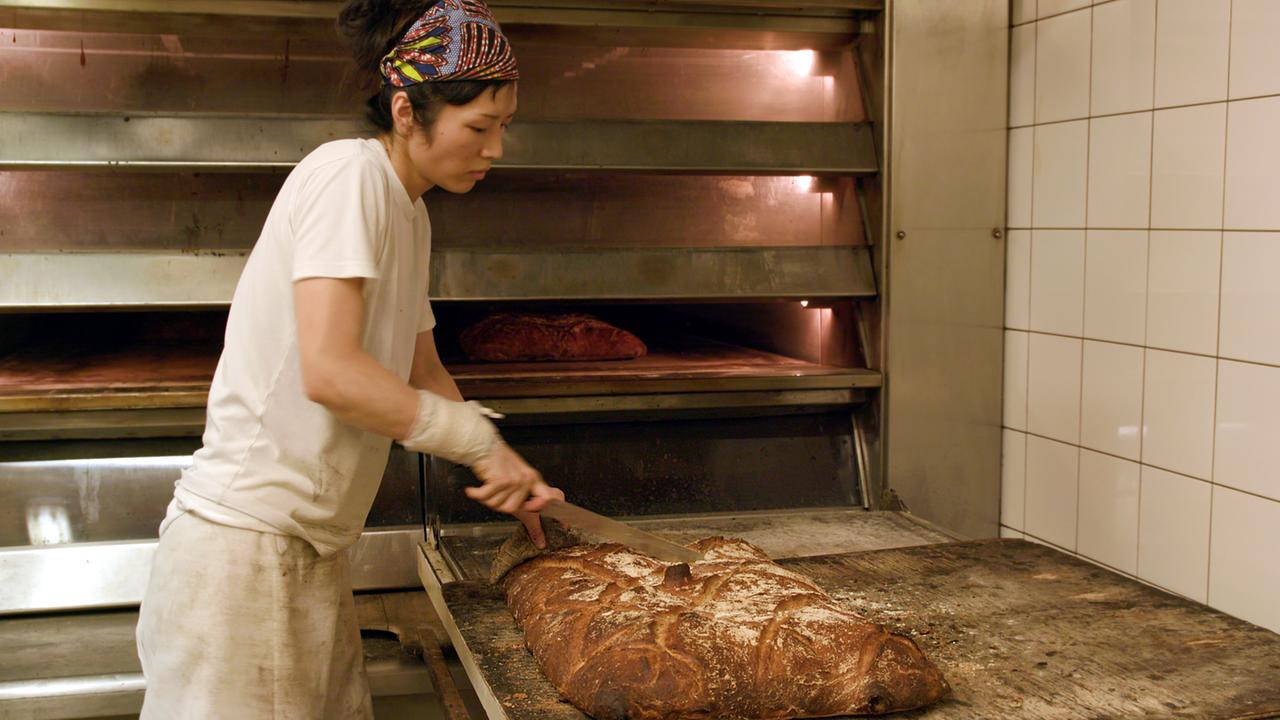 Eine Frau nimmt Brot aus einem Ofen. Szene aus dem Film “Brot" von Harald Friedl.