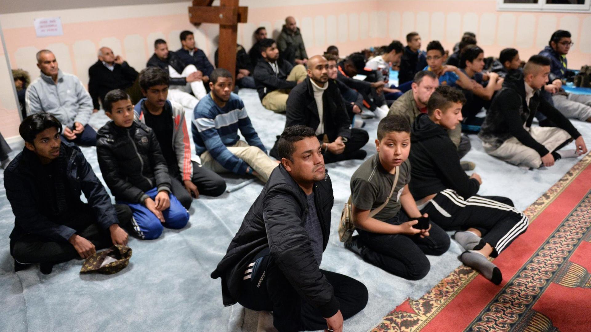 Menschen sitzen auf dem Boden einer Moschee.
