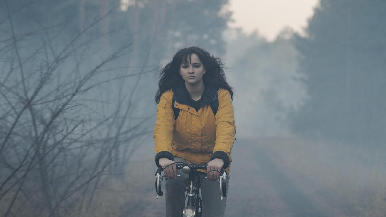 Lisa Vicari in der Rolle der Martha Nielsen, fährt in einer gelben Jacke Fahrrad durch den Wald. Lisa Vicari in der Rolle der Martha Nielsen, fährt in einer gelben Jacke Fahrrad durch den Wald.
