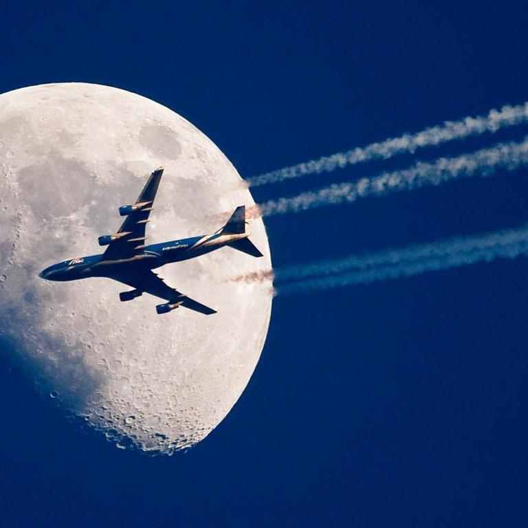 Ein Flugzeug fliegt über dem brandenburgischen Sieversdorf (Oder-Spree) scheinbar ganz nah am Mond vorbei. 