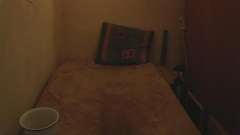 Ein beflecktes Bett mit Kopfkissen und Schüssel in einem dunklen Zimmer.