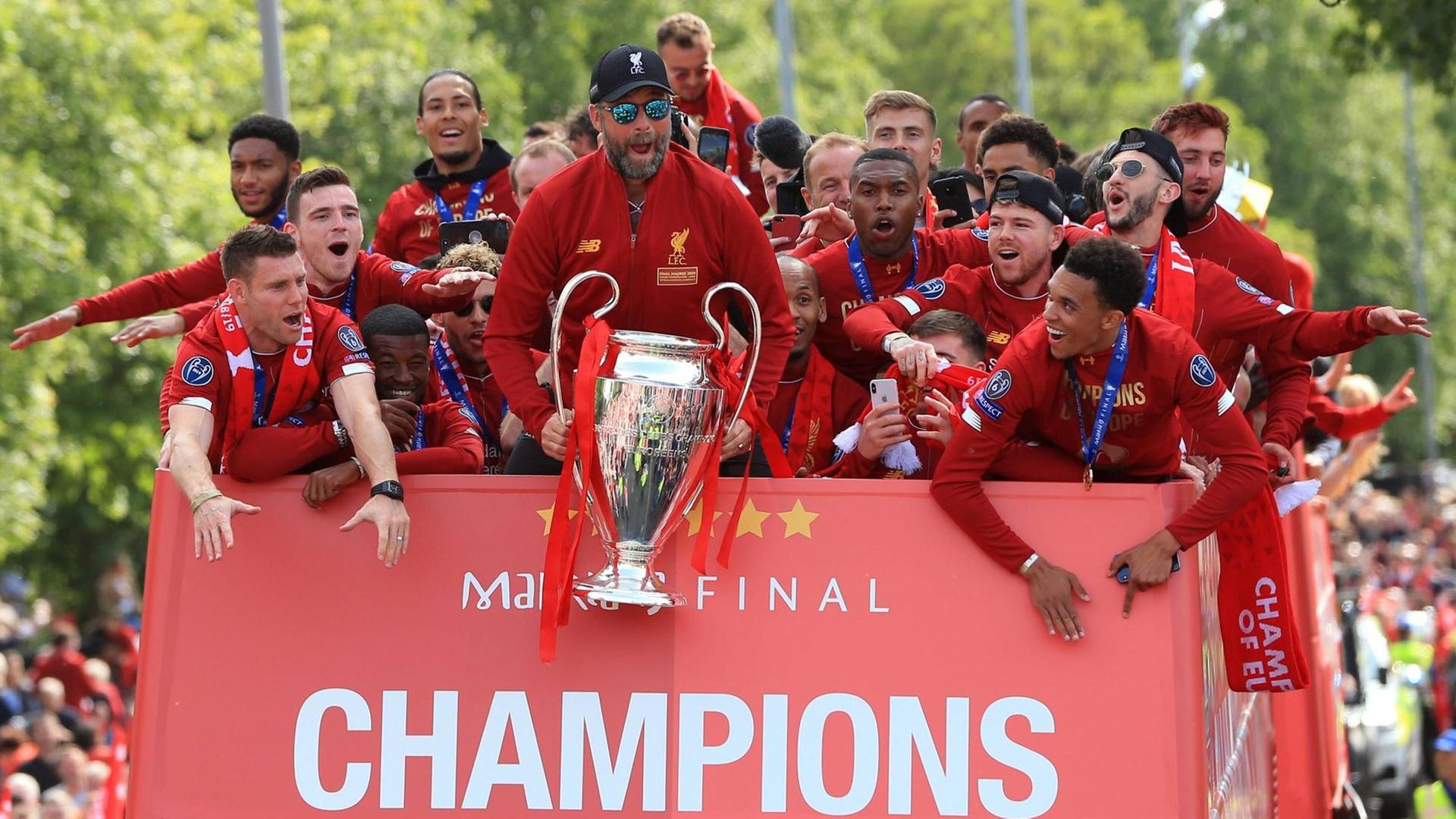 Trainer Jürgen Klopp feiert mit Spielern und Fans den Sieg der Champions League. Klop hält den Pokal in den Händen, die Spieler jubeln.
