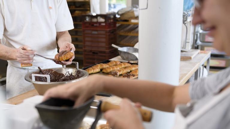 In einer Bäckerei werden Croissants mit Schokolade bestrichen.